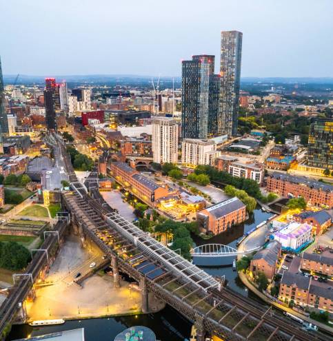 Manchester United Kingdom aerial shot of modern buildings with lots of counstruction in the central area of the city with historic canals and railways in the foreground by night